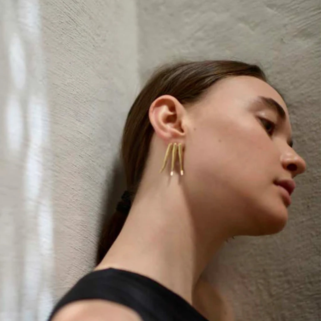 Woman wearing gold earrings against a neutral background