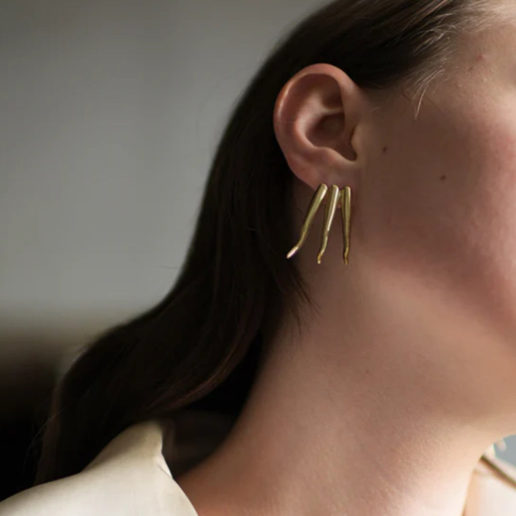 Gold earring worn by a person with a neutral background