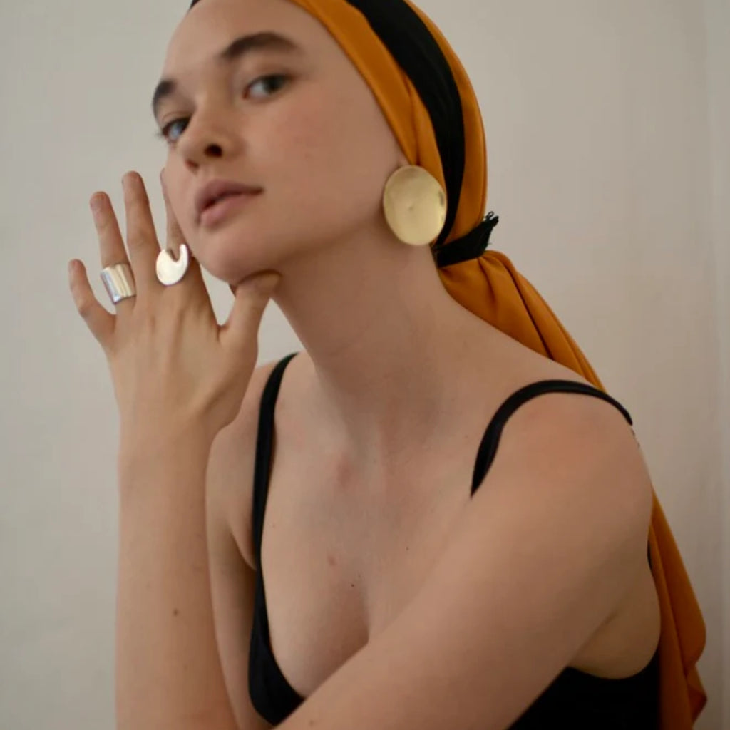 Woman wearing gold earrings and a ring, with a plain background