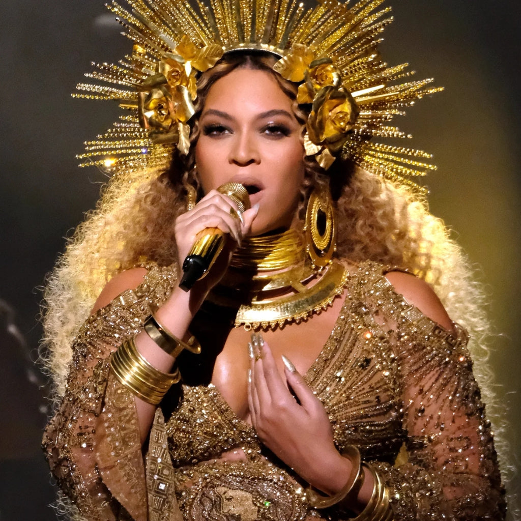 Person in a gold outfit with a large, ornate headpiece holding a microphone.