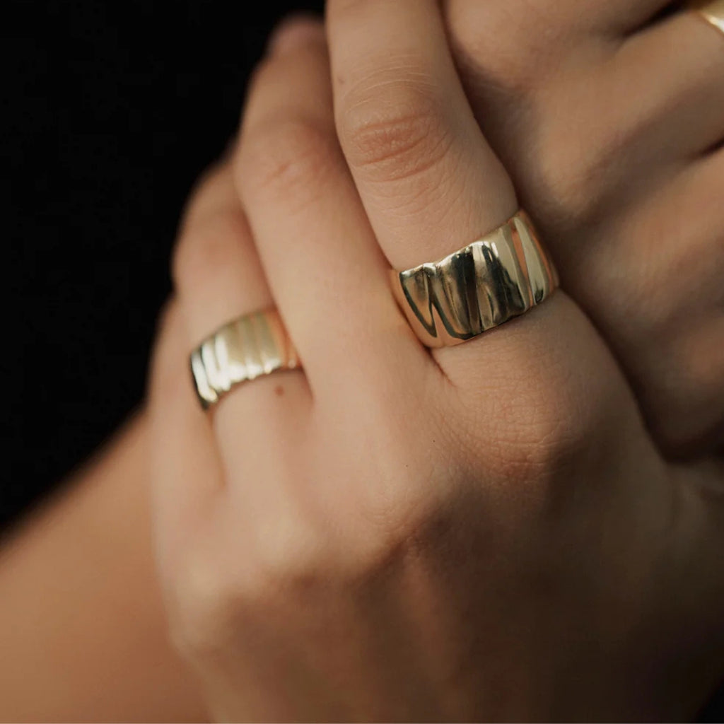 Close-up of a hand wearing two gold rings on a dark background