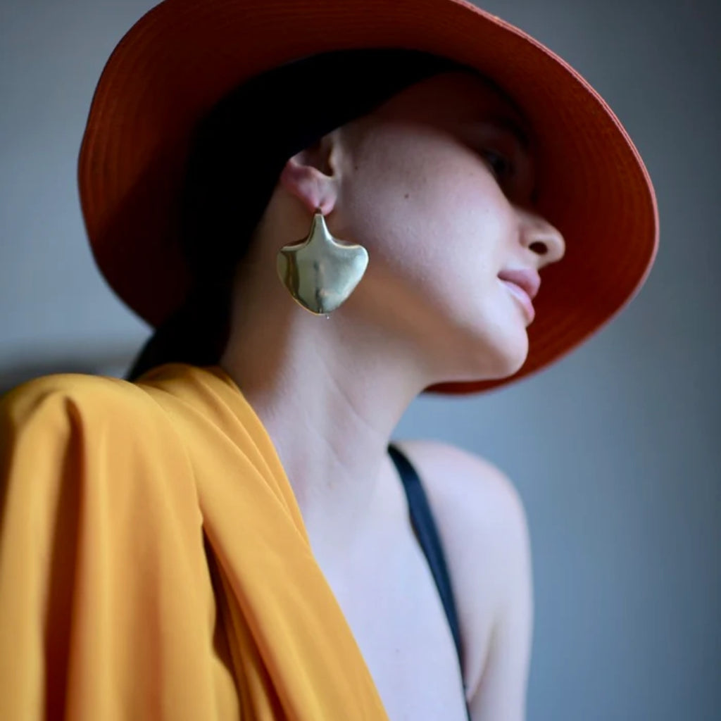 Woman wearing a red hat and gold earring against a gray background