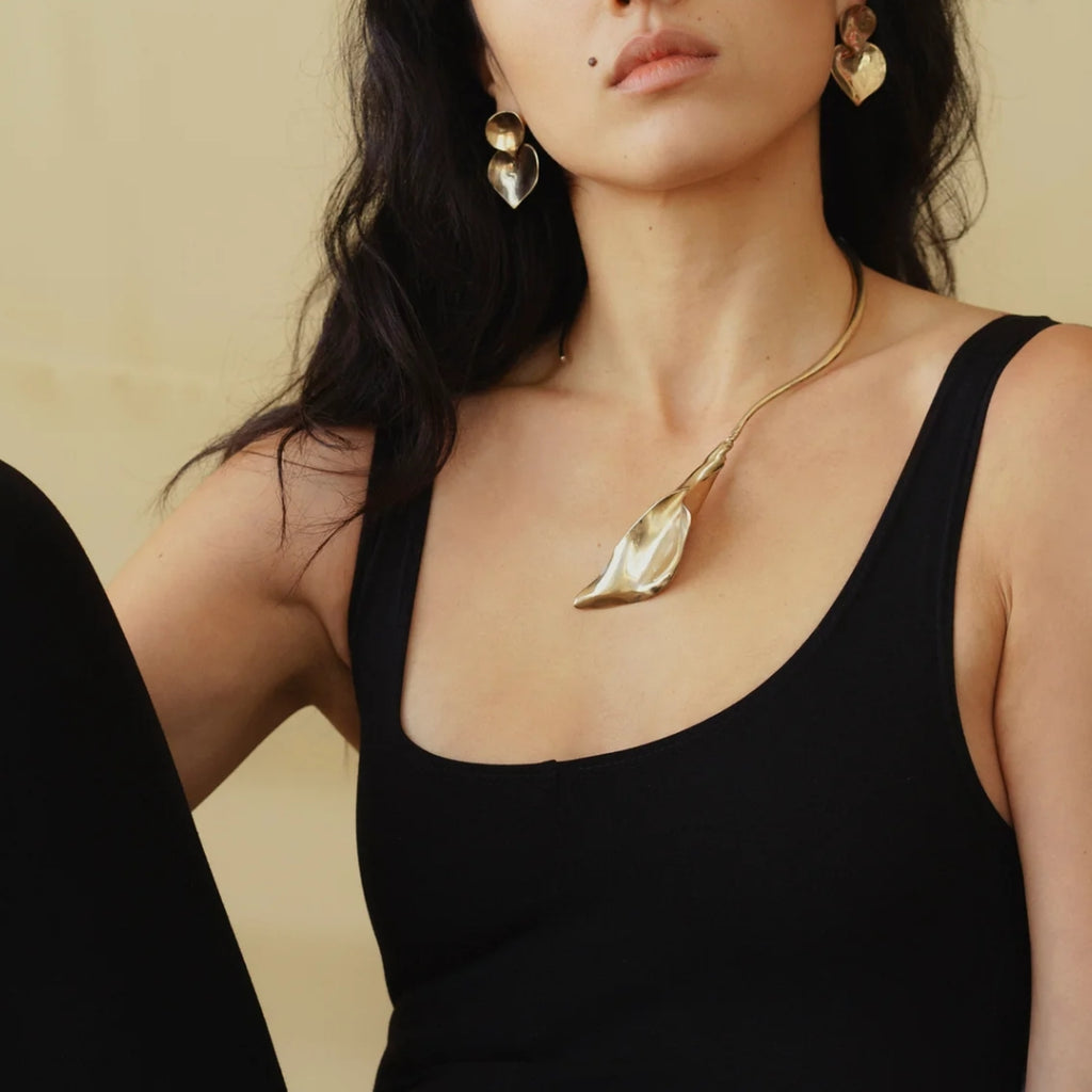 A model wearing a gold calla lily necklace and matching earrings against a neutral background.