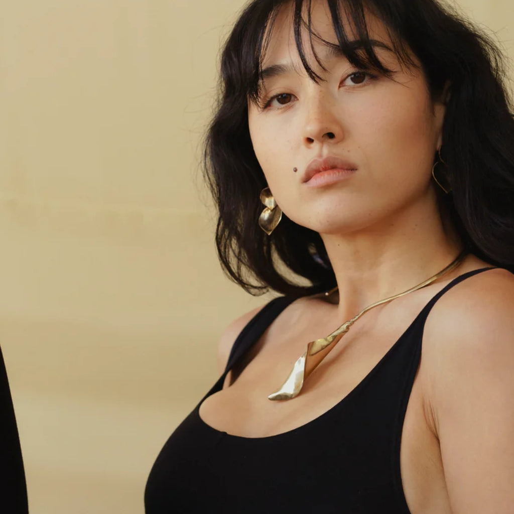 A model wearing a gold calla lily necklace and matching earrings, exuding confidence against a soft background.