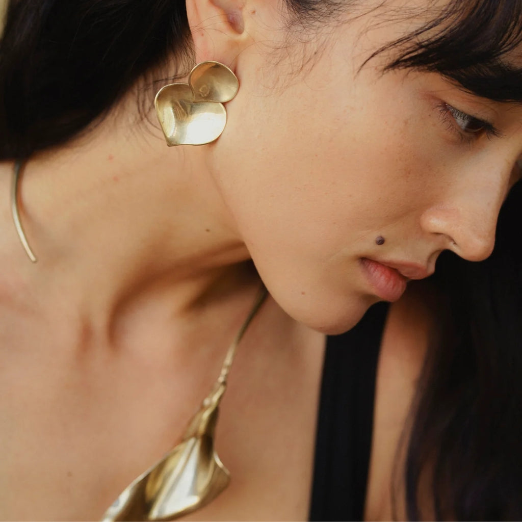 A close-up of a model wearing gold Birch earrings, highlighting their sculptural design against a soft background.