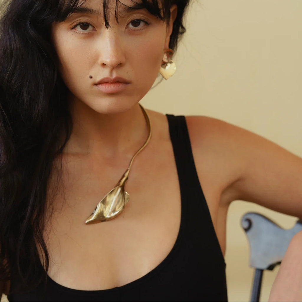 A model confidently showcasing gold calla lily earrings and a matching necklace against a neutral background.