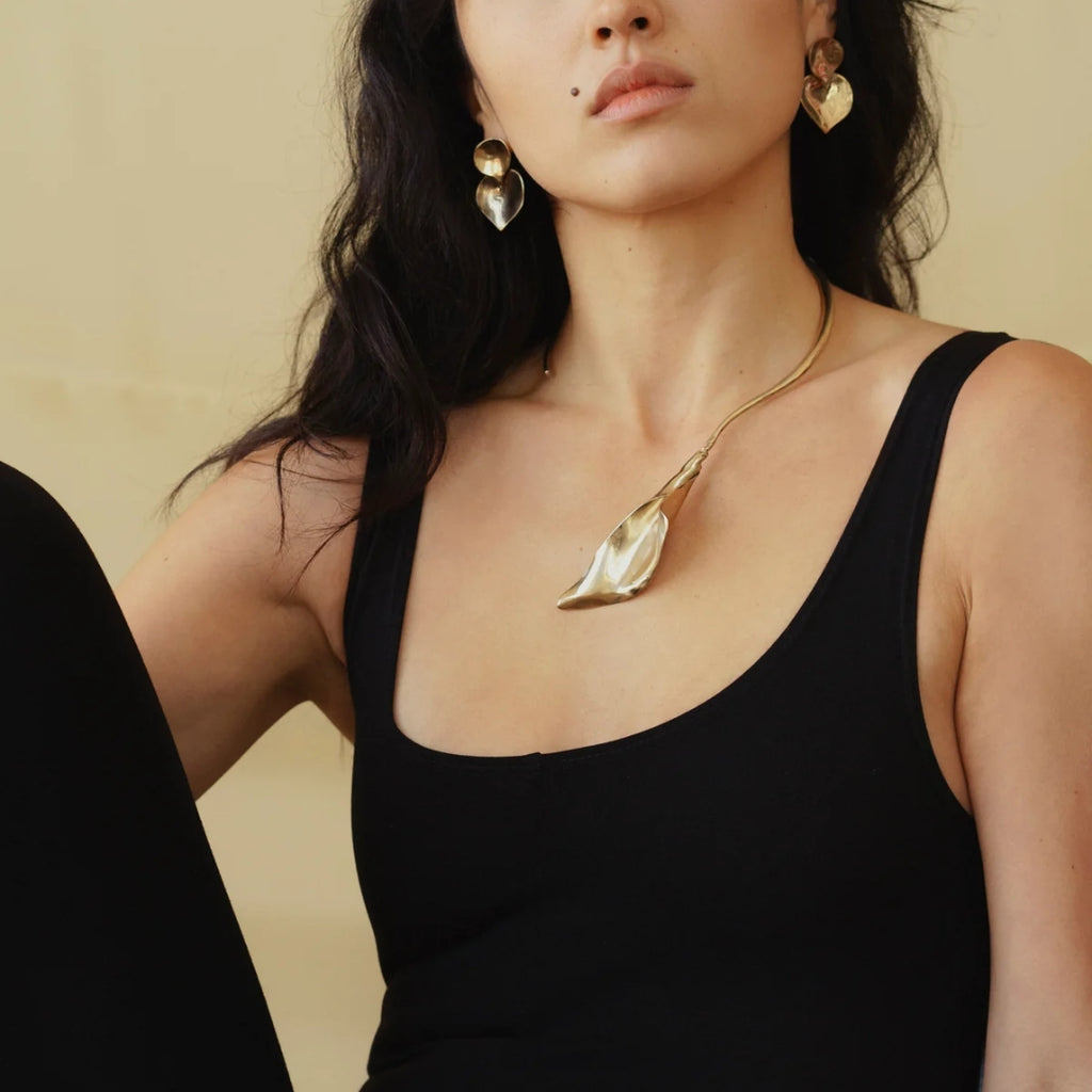 A model wearing a gold calla lily necklace and matching earrings, exuding elegance against a soft beige background.