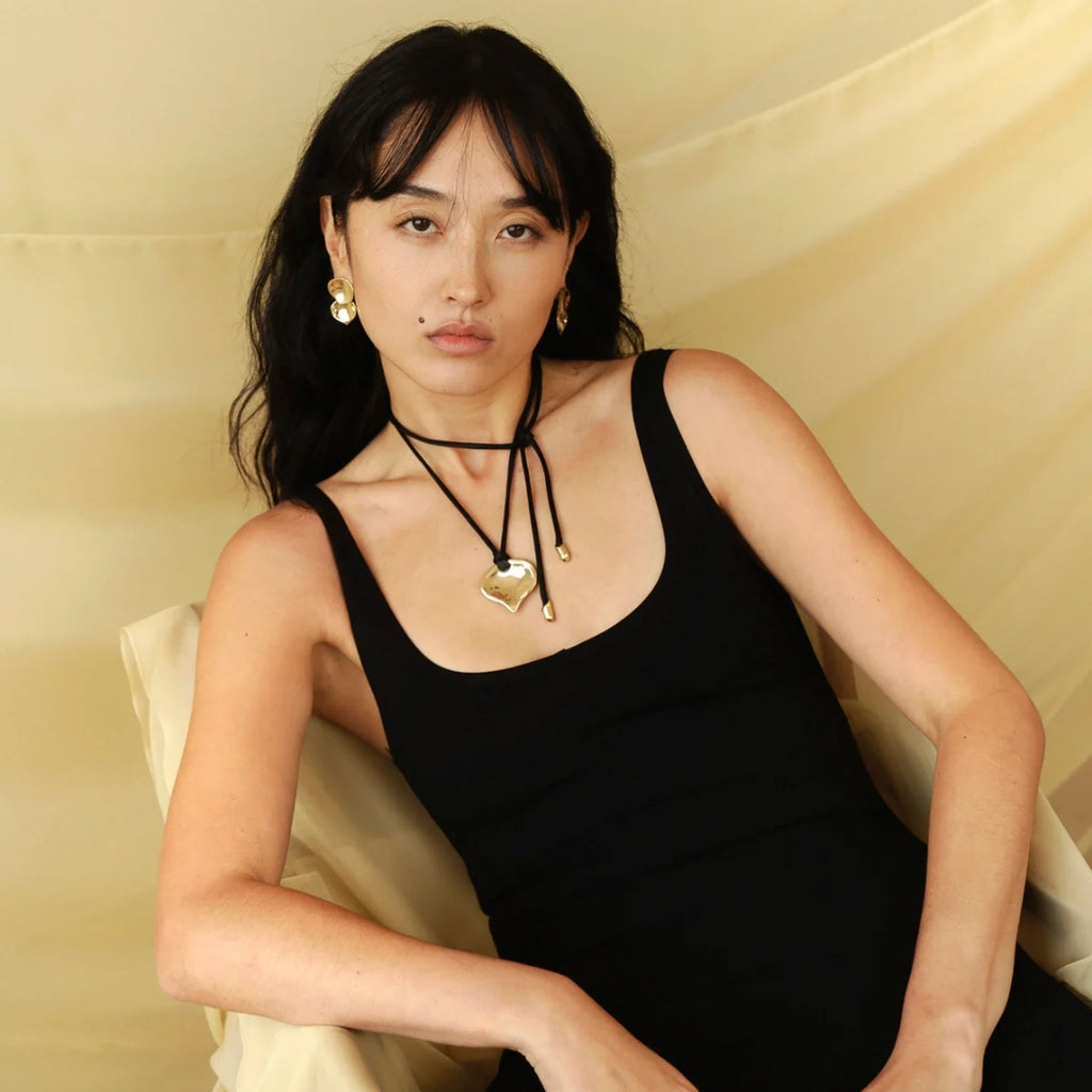 Woman wearing a black tank top with gold necklaces against a beige background