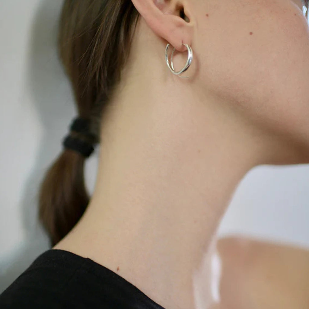 Close-up of a person wearing a silver hoop earring with a neutral background