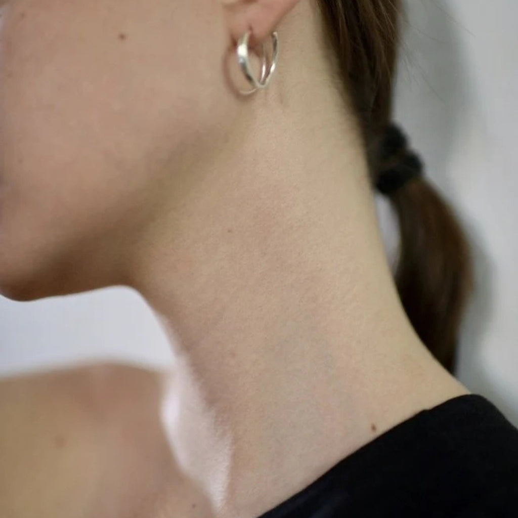 Close-up of a person wearing silver hoop earrings with a blurred background