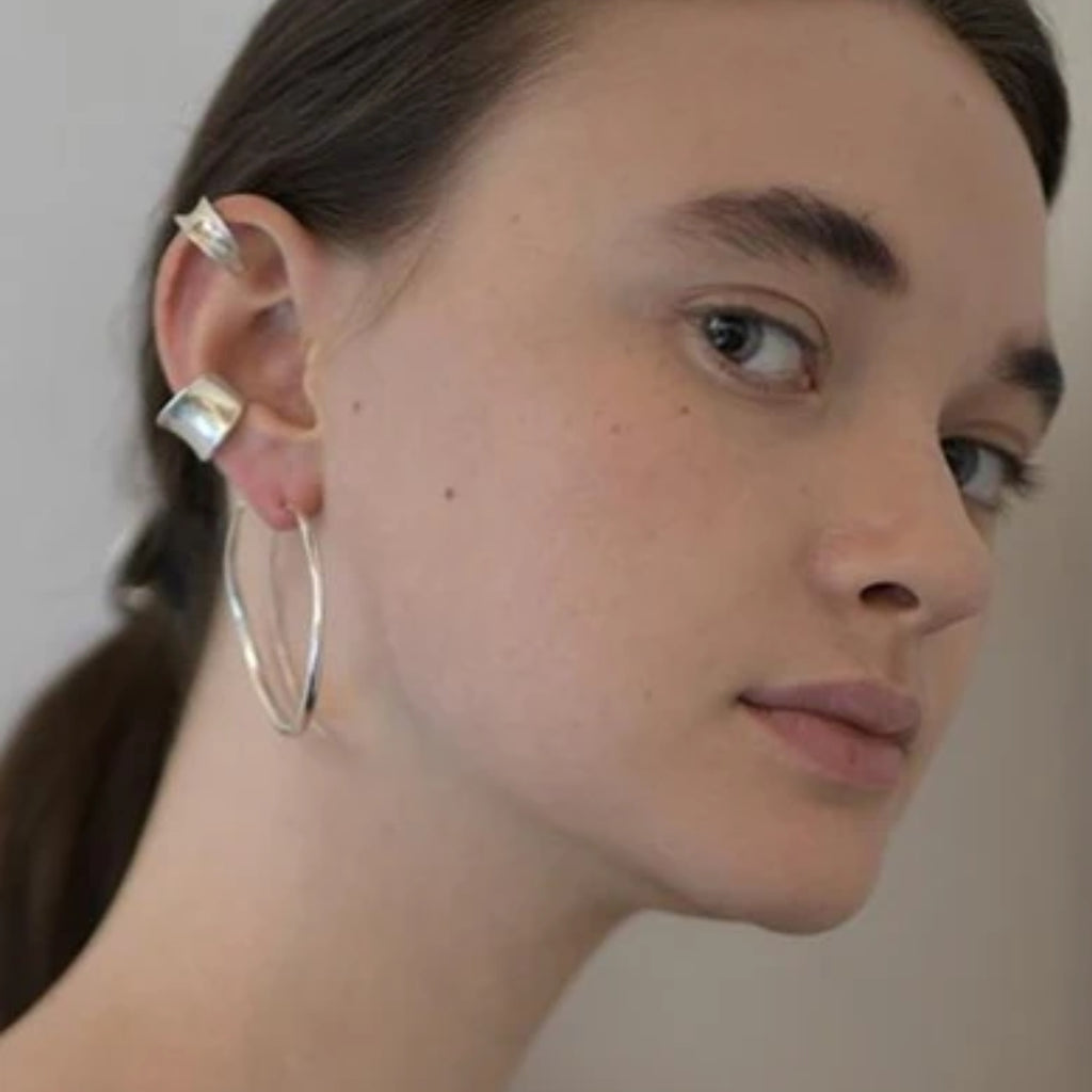 Close-up of a person wearing silver hoop earrings with a neutral background