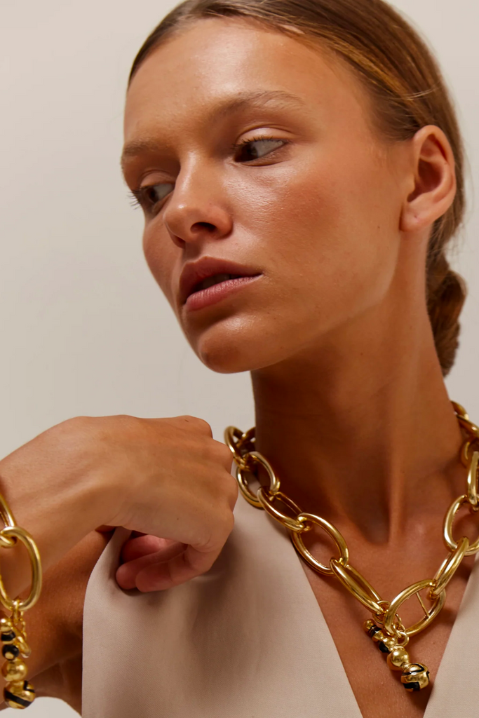 The Agios necklace is a stunning tribute to Greek culture, featuring gold-plated elements, an enameled clasp, and sustainable production in Spain.