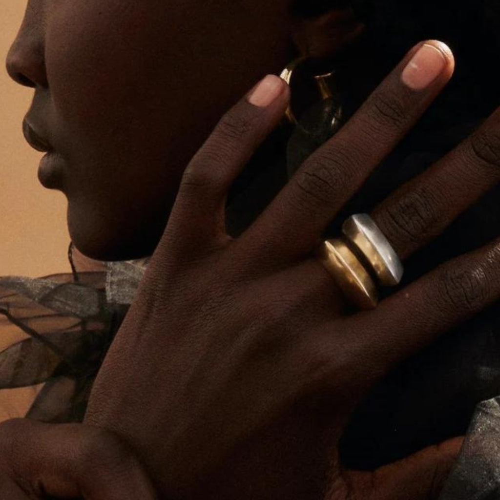 Close-up of a person's hand with gold rings on a neutral background