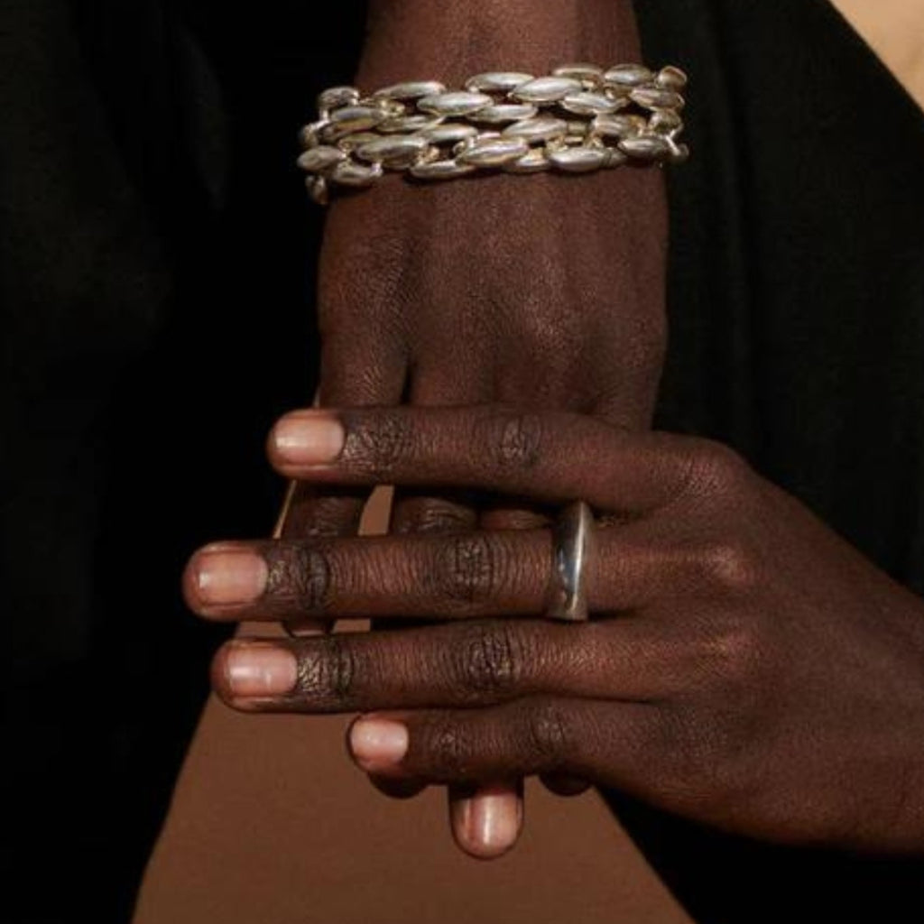Close-up of hands with a silver chain bracelet and ring on a dark background