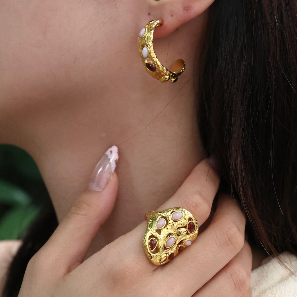 Close-up of a person wearing gold hoop earrings and a matching ring.
