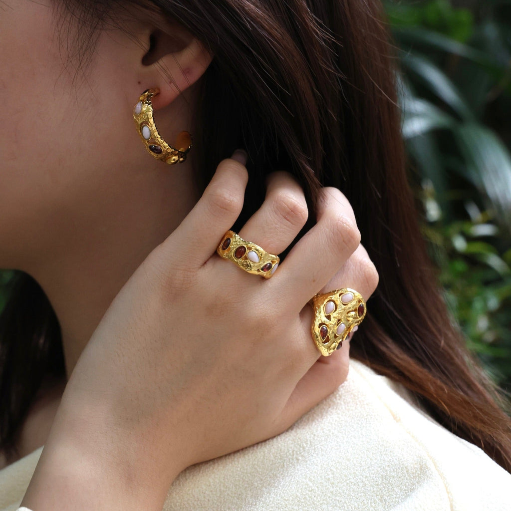 Close-up of a person wearing gold hoop earrings and rings with a blurred green background