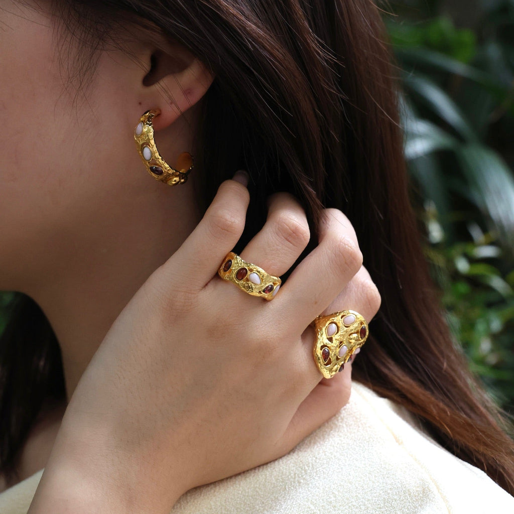 Close-up of a person wearing gold hoop earrings and rings with a blurred green background