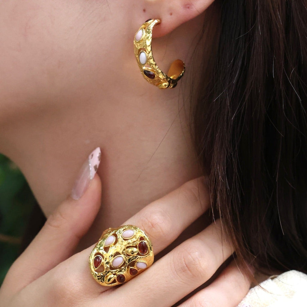 Close-up of a person wearing gold hoop earrings and a ring with a green background