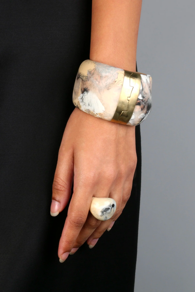 Elevate any outfit with the stunning Resin Bold Stone Cuff in Sandy Pearl by Dinosaur Designs, featuring a unique swirl pattern and brass hinge.