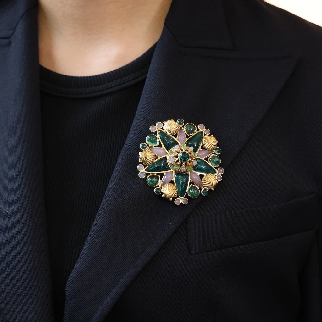 Close-up of a person wearing a black blazer with a decorative brooch featuring green and gold elements.