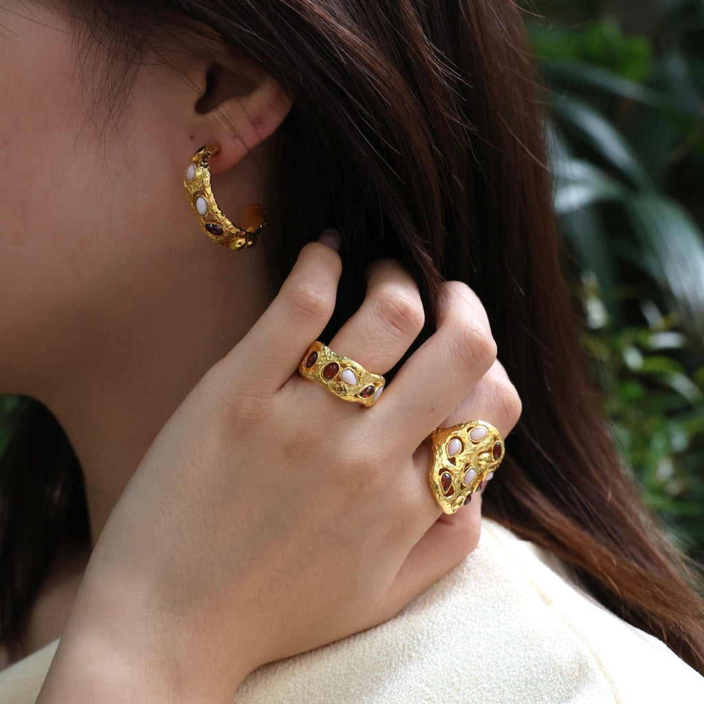 Close-up of a person wearing gold hoop earrings and rings with a blurred green background
