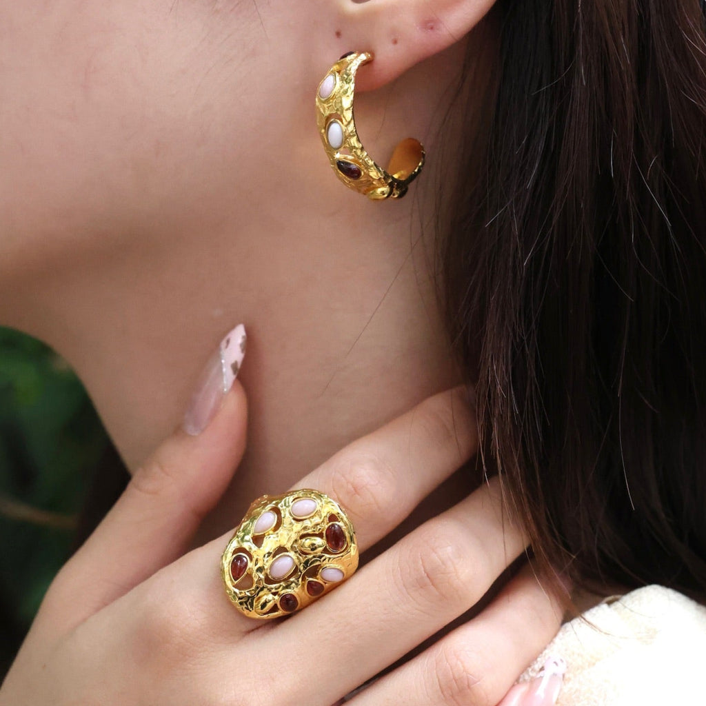Close-up of a person wearing gold hoop earrings and a ring with a green background