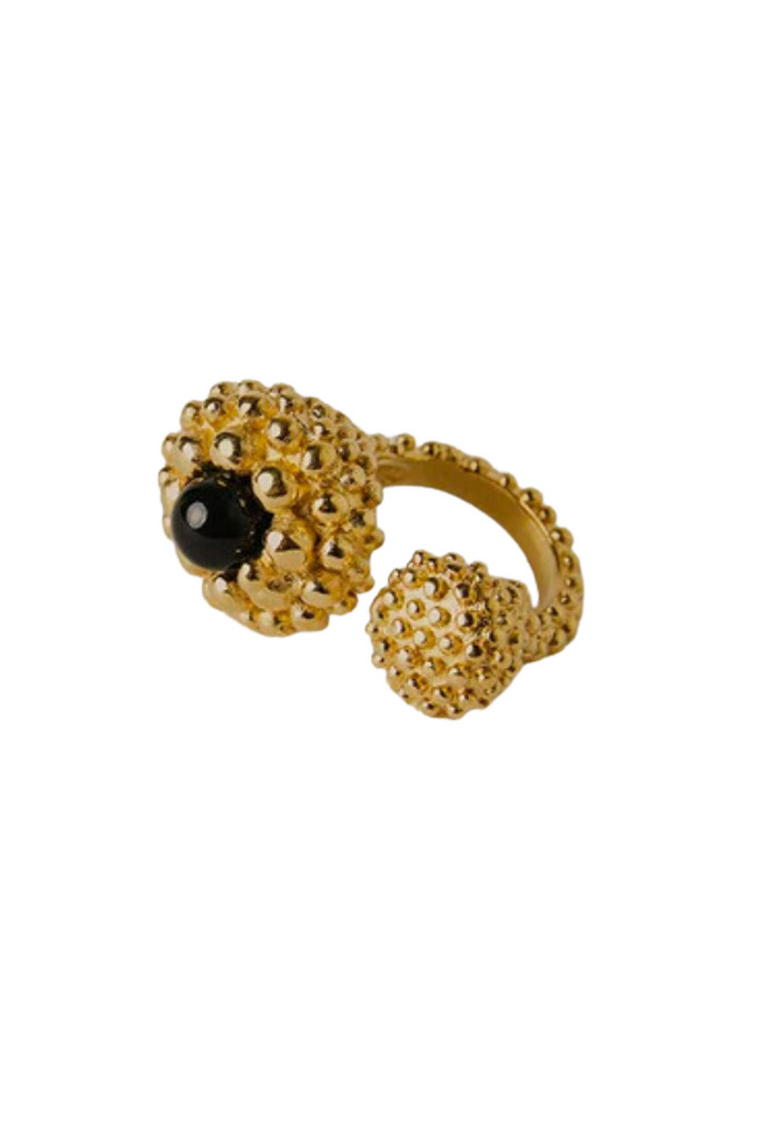 The Karpos Ring, designed by Paola Sighinolfi in collaboration with Patrizia Casarini, is a handcrafted black stone ring adorned with gold-plated metal bubbles inspired by the Mediterranean coast, evoking the natural beauty of the Cadaqués coves and creating a timeless and contemporary piece of jewelry.