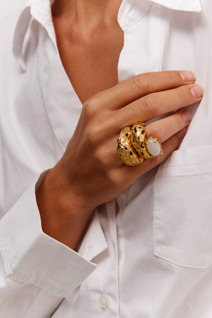 Paola Sighinolfi's Mayge ring is a handcrafted statement piece featuring a claw-set moonstone cabochon on a textured open band plated in 18kt gold, providing a unique and elegant touch to any outfit.