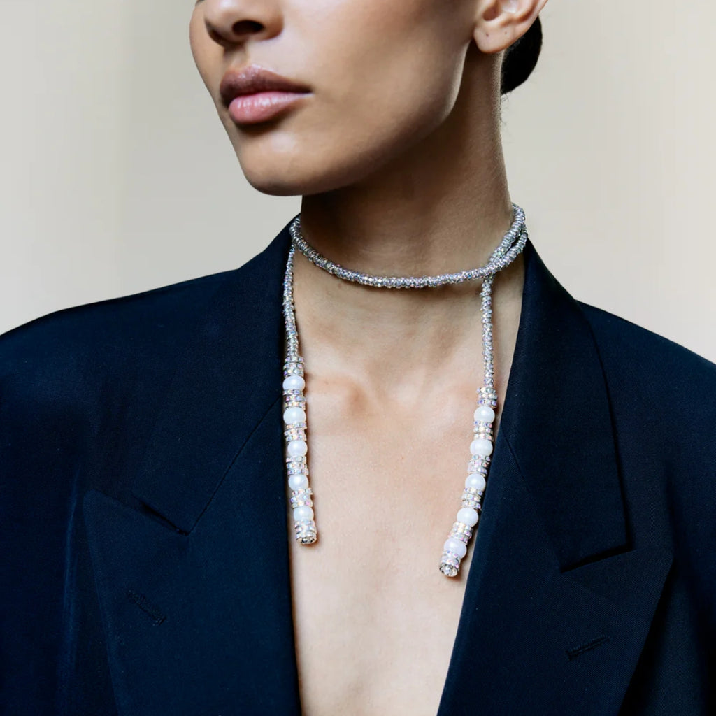 Woman wearing a pearl necklace with a dark blazer against a neutral background