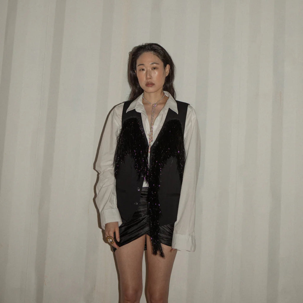 Person wearing a black sequin vest over a white shirt with a plain background