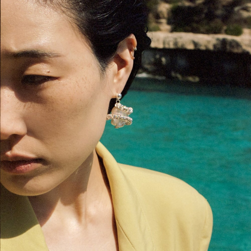 Close-up of a person wearing earrings with a blurred natural background