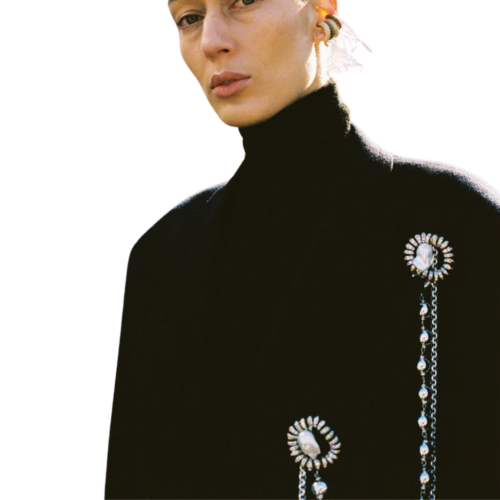 Person wearing a black turtleneck with a decorative brooch on a white background