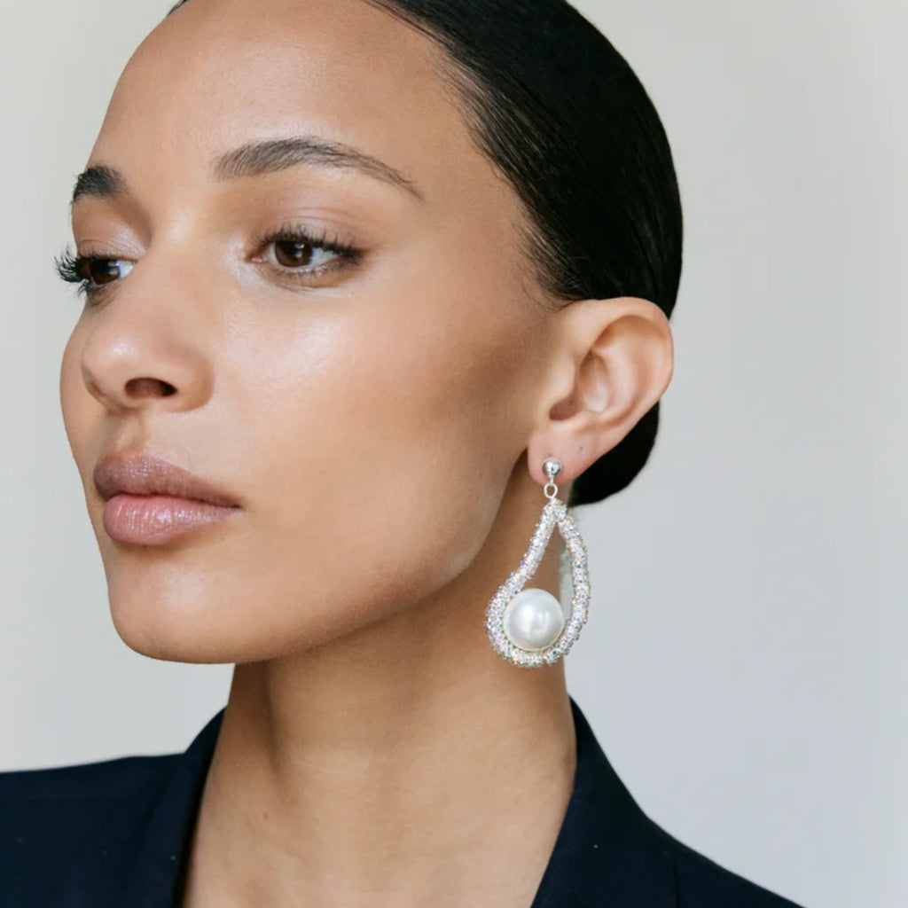 Close-up of a woman wearing a pearl earring against a neutral background