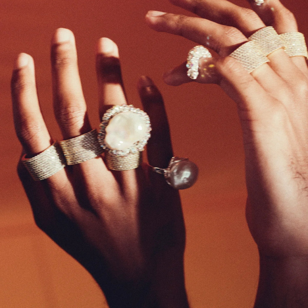 Two hands wearing multiple gold rings with various designs on a red background