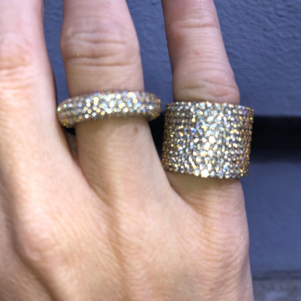 Two gold rings with gemstones on a person's fingers against a dark background