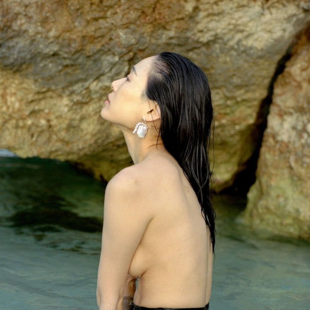 Woman with long black hair standing by large rocks near water