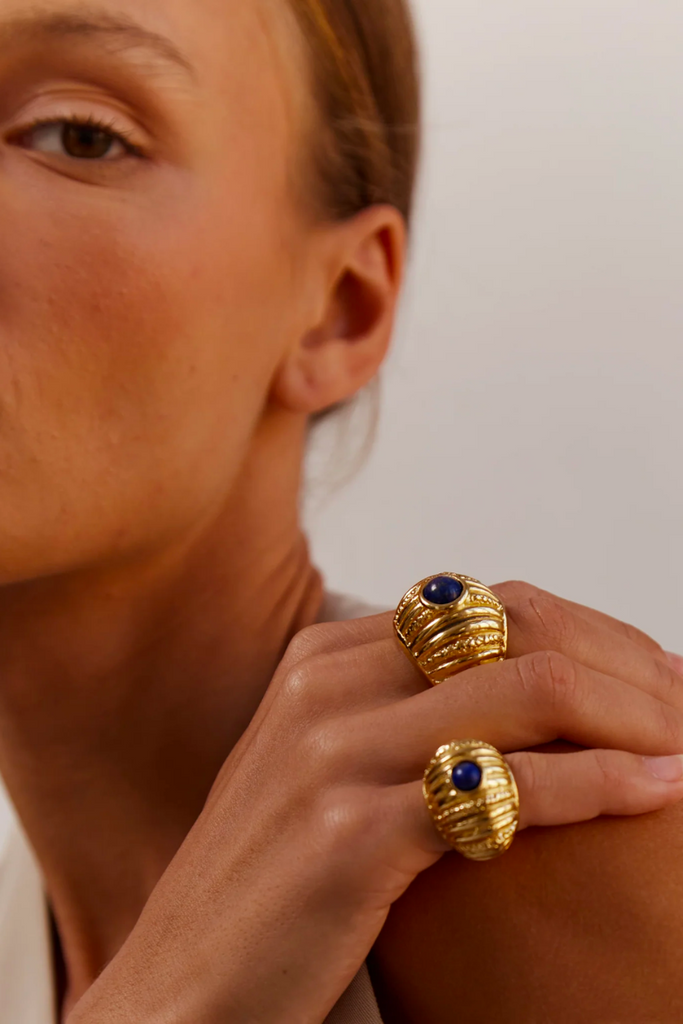 The Reef Ring from Paola Sighinolfi is a handcrafted, 18kt gold-plated organic ring inspired by coral gardens and featuring a blue stone that exudes regal elegance and tranquility, making it a timeless and elegant accessory perfect for any formal occasion.