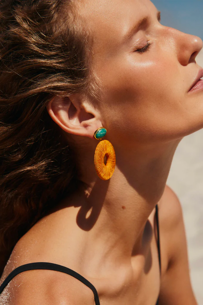 Inspired by a tidal lagoon along the Portuguese coast, the Ria Formosa Earrings by Lizzie Fortunato feature gold-plated brass, amazonite stone tops, and amber silk cord woven hoops, making them a playful and unique statement piece for any occasion.